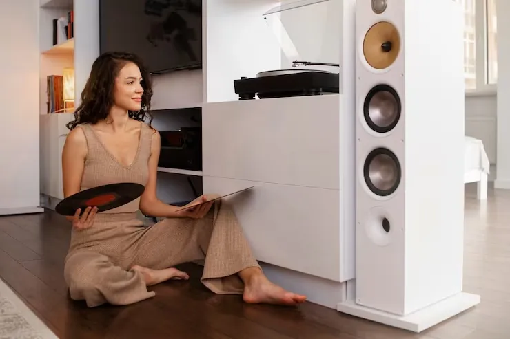 Persona sentada en el suelo escuchando música junto a un tocadiscos y un altavoz de columna, imagen ilustrativa